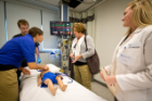 A nursing student and resident work with simulation specialists on a scenario involving an injured child and distraught parents.
