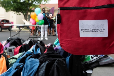 Several backpacks lined up on the ground with one that has a memorial school drive sticker on it. 