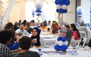 People sitting at tables with blue and white balloons. 