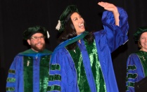 Person waving as they walk the stage during commencement. 