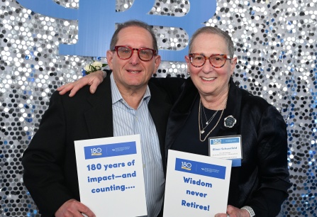 Event attendees holding up a sign with text: 180 years of impact and counting and wisdom never retires. 