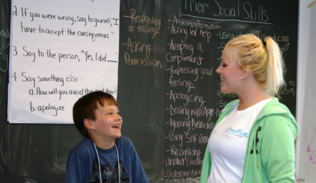 Instructor talks to child in front of chalkboard.