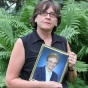 A photo of Mary Brennan-Taylor in a garden, holding a framed picture of her mother, Alice Brennan. 