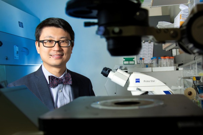 Dr. Hu sitting by a microscope.