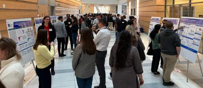 Crowd gathered in the atrium looking at posters. 