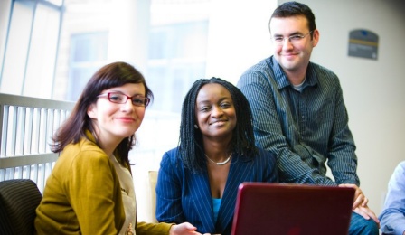 Two female students and one male student sitting in front of a laptop. 