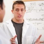 Student explaining his research to a faculty mentor in front of a white board. 