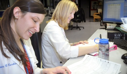 Two female medical students in white coats filling out paperwork. 