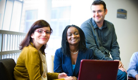 Three students sitting in front of a laptop computer. 
