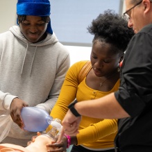 High school students being guided on a procedure with a mannequin by an instructor. 