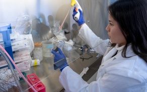 Biochemistry student next to microscopes in a lab coat. 
