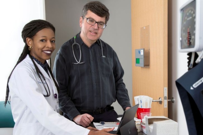 Medical student in white coat with instructor working over a computer monitor. 
