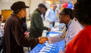 Two people shaking hands over a community event table. 