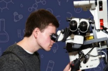 Young man with short hair looks through a microscope. 