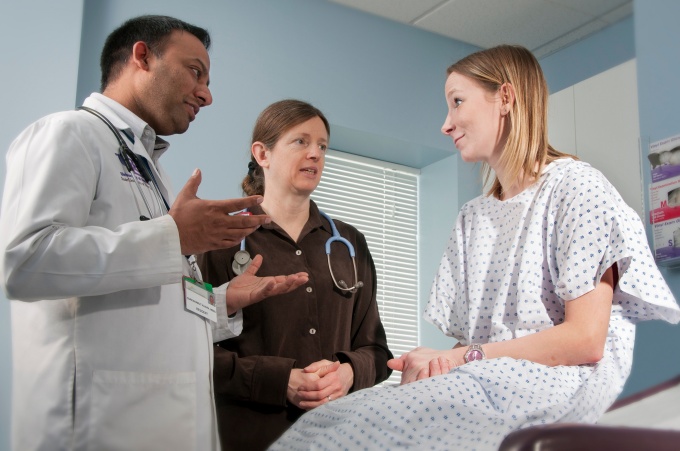 A patient sits in a doctor's office with two people. 