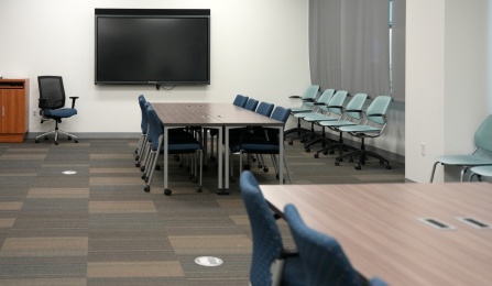 A view of the debrief rooms with a large TV screen and two blocks of tables with chairs at them. 