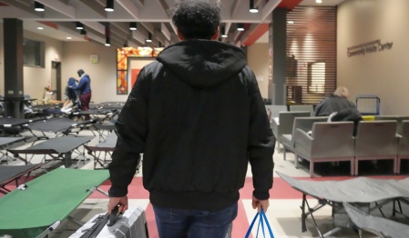 UB student carrying supplies into Buffalo shelter where numerous cots are set up. 